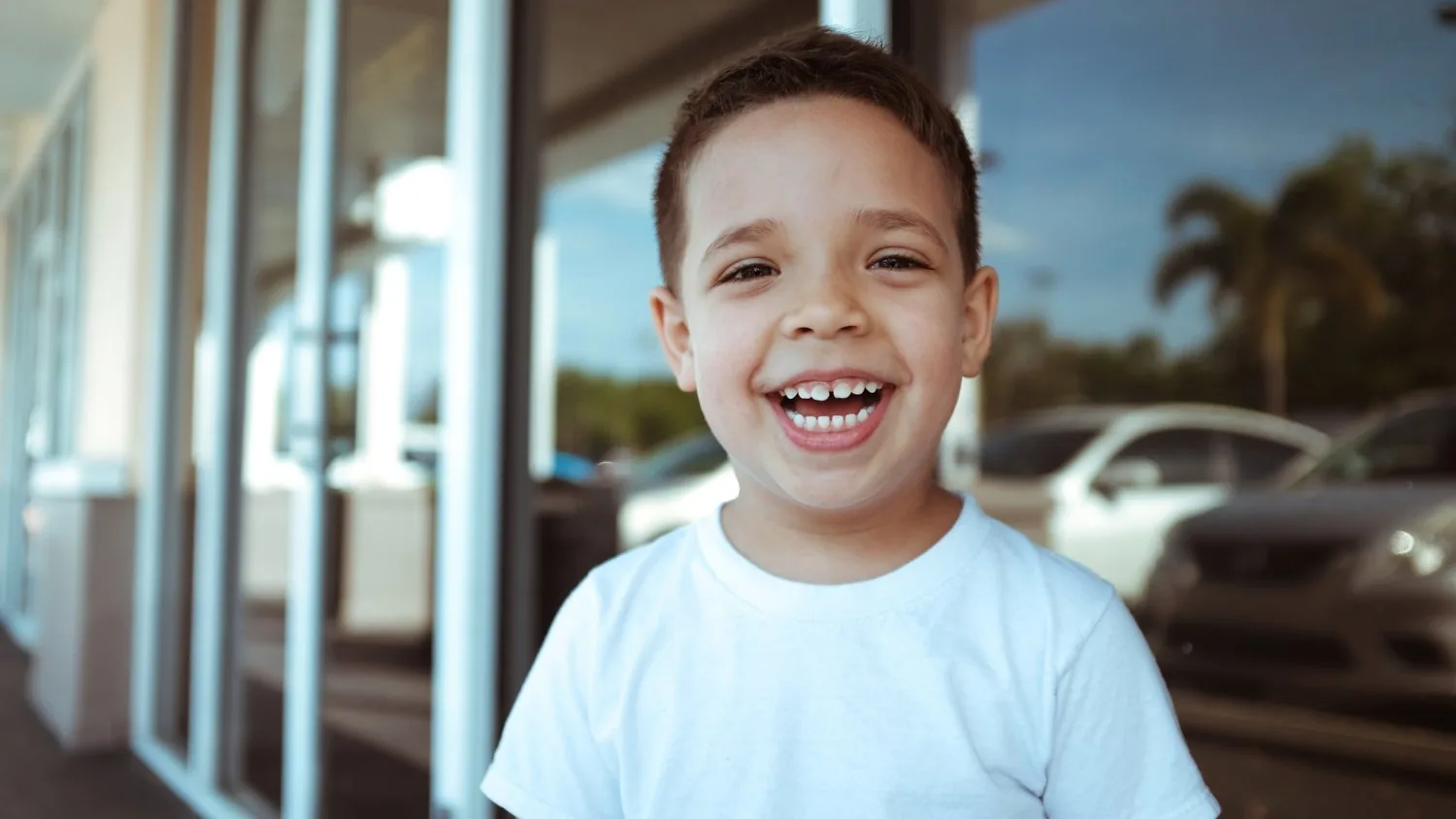 A smiling child wearing a white t-shirt showing their teeth.