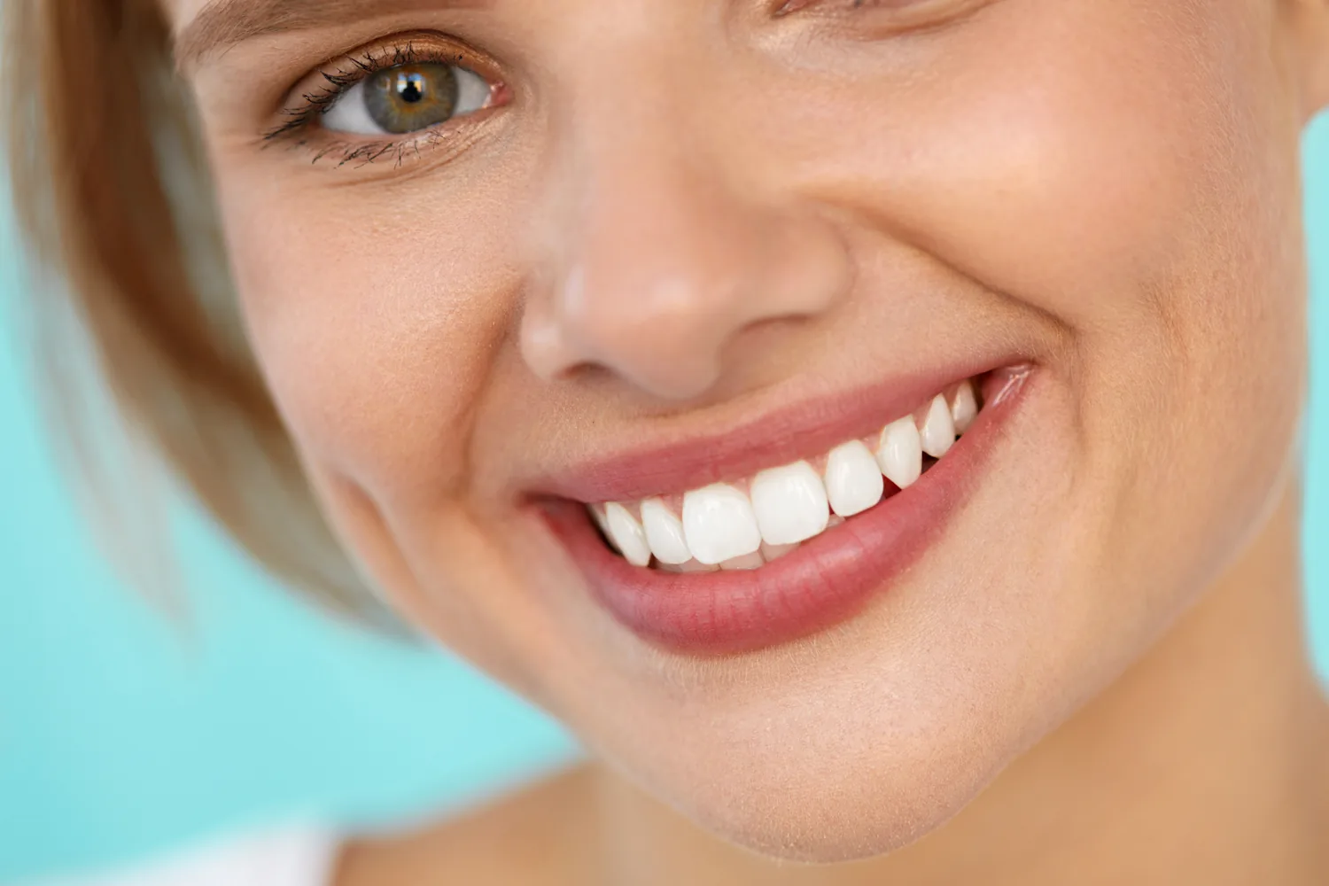Smiling person showing straight, white teeth on a light blue background.